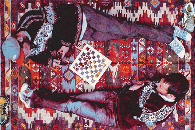 שני אנשים משחקים שח מט בשכיבה על שטיח צבעוני 
